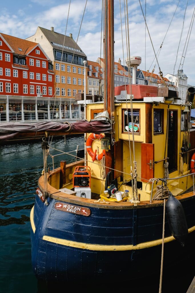 A vibrant boat docked at Nyhavn harbor in Copenhagen, Denmark, under a sunny sky.