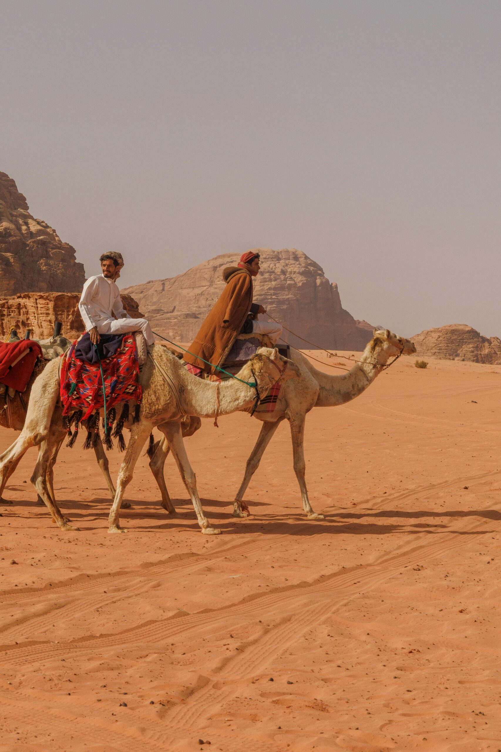Two men riding camels traverse the vast desert landscape near Aqaba, Jordan.
