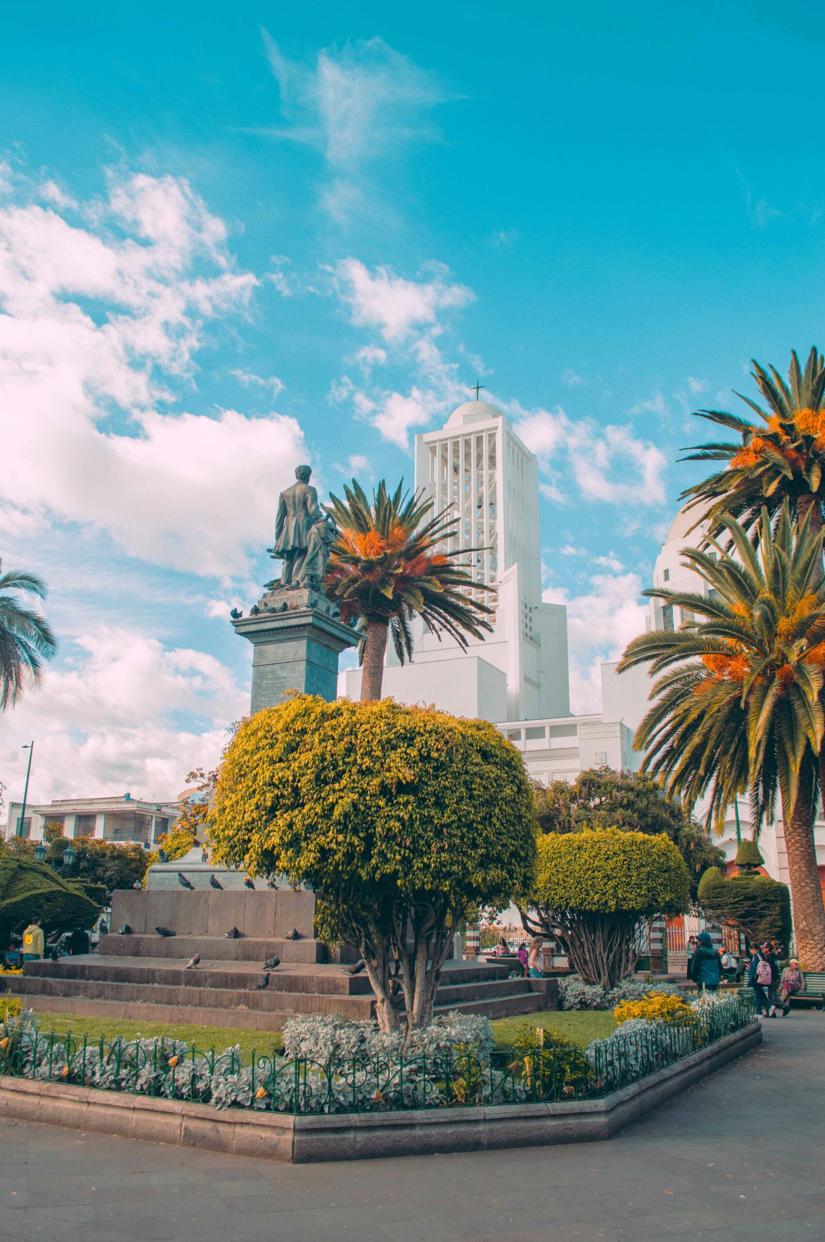 Beautiful sunny day in Ambato's central square with statue and palm trees.