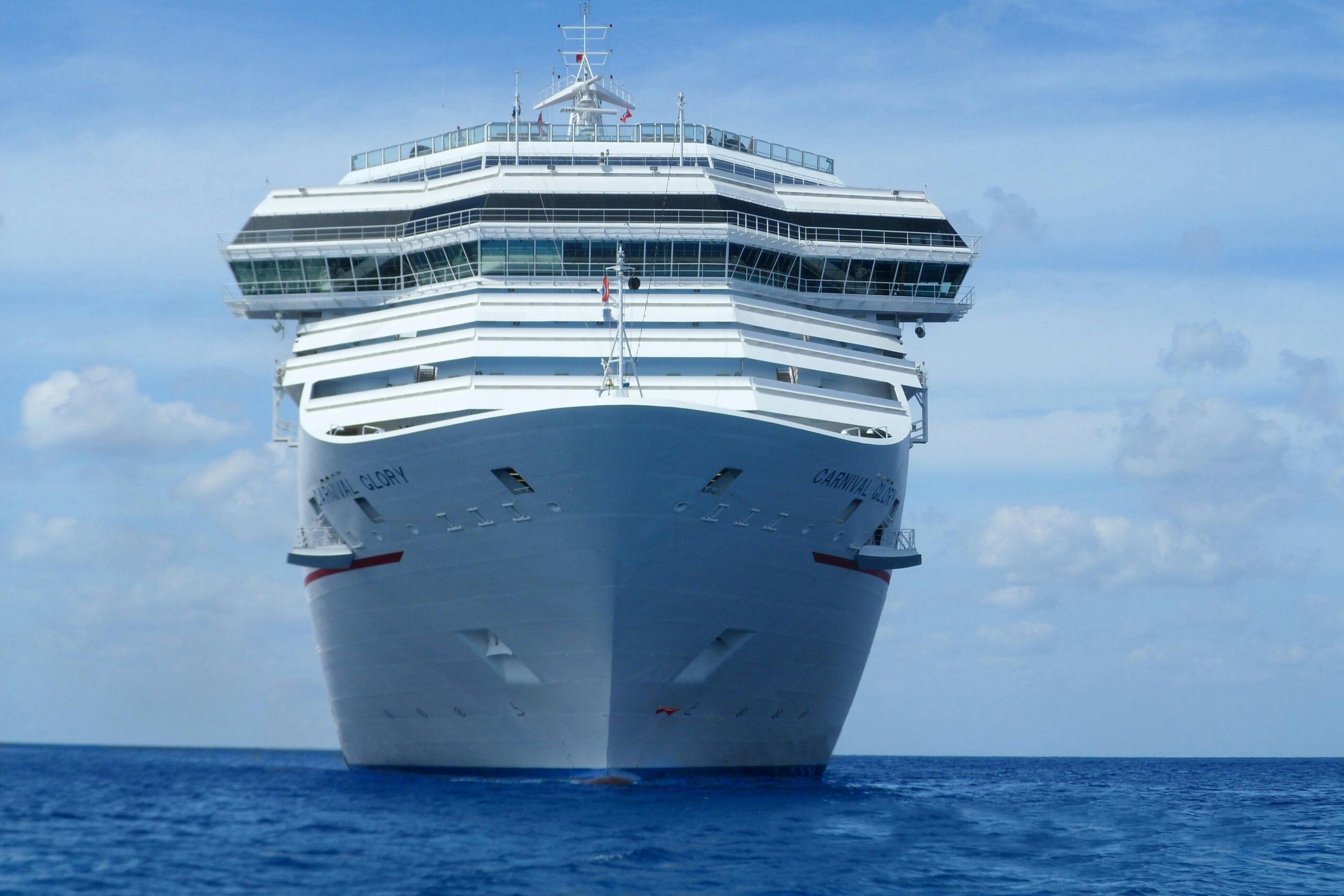 Front view of a large cruise ship on a calm blue ocean under a clear sky.
